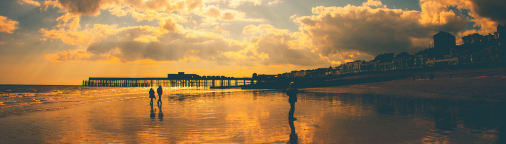 sunset on a beach with people and pier silhouetted